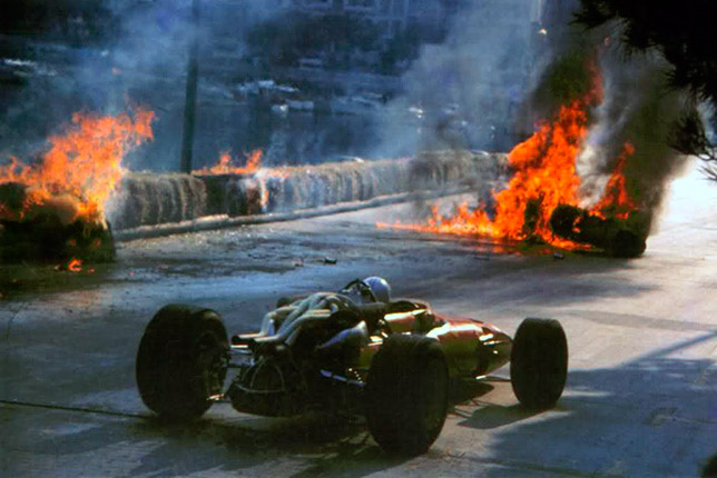 Крис Эймон проезжает мимо горящей машины своего напарника Лоренцо Бандини